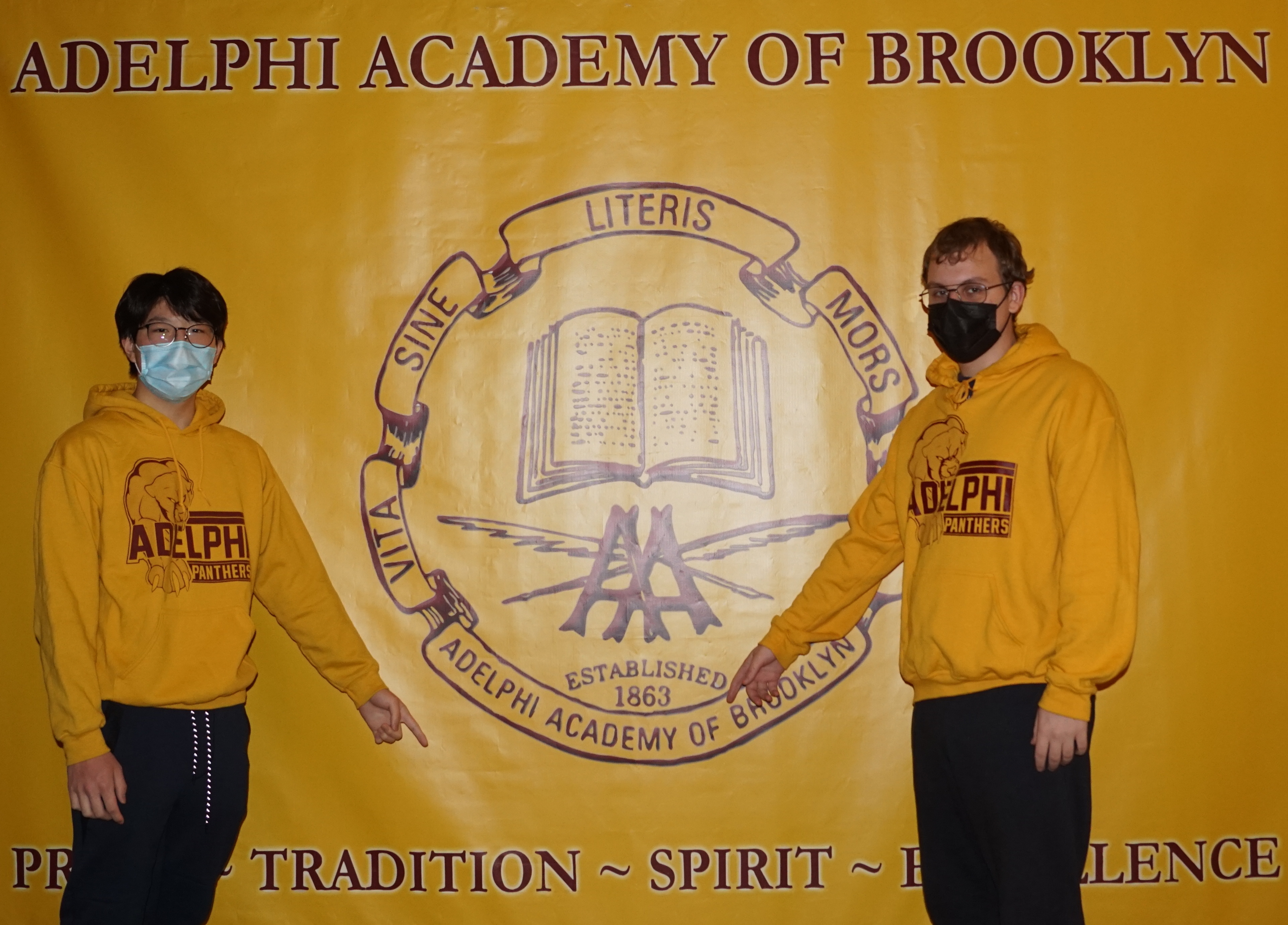 Class of 2021 members William and Boris point to key words on Adelphi's banner.
